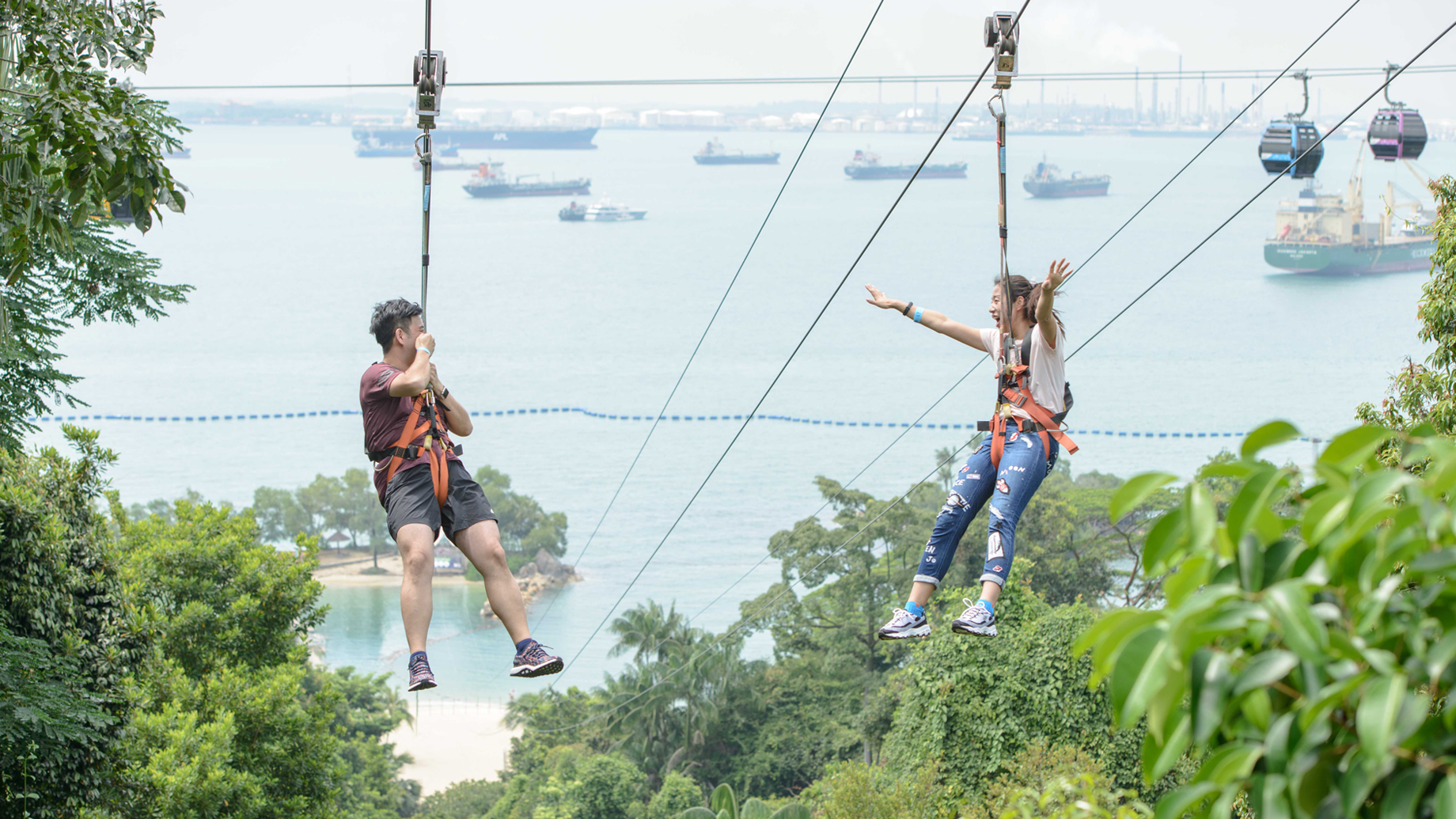 A couple on a zipline descending at great speed toward Siloso Beach